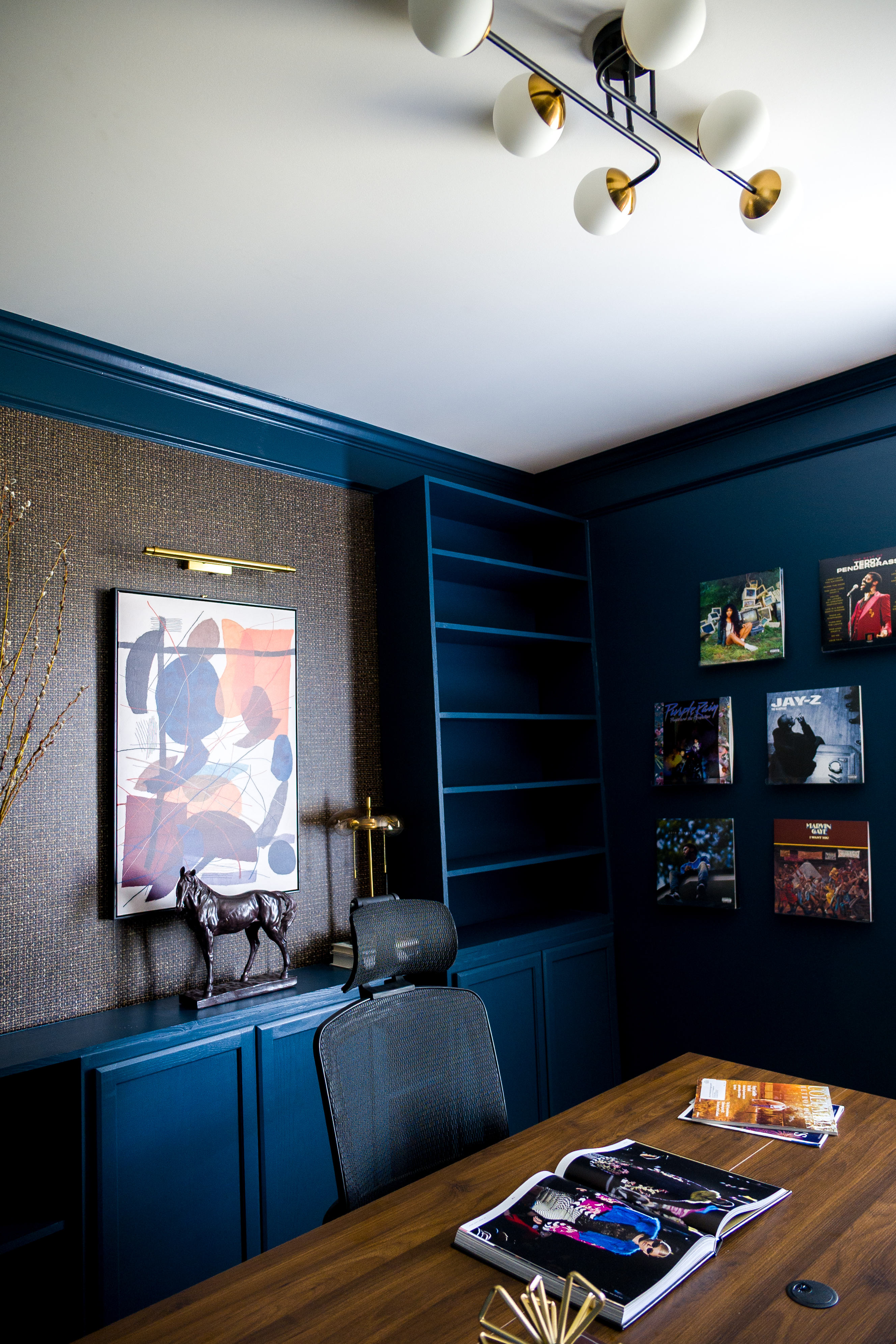 Full home office with brass chandelier, teal walls, and record gallery